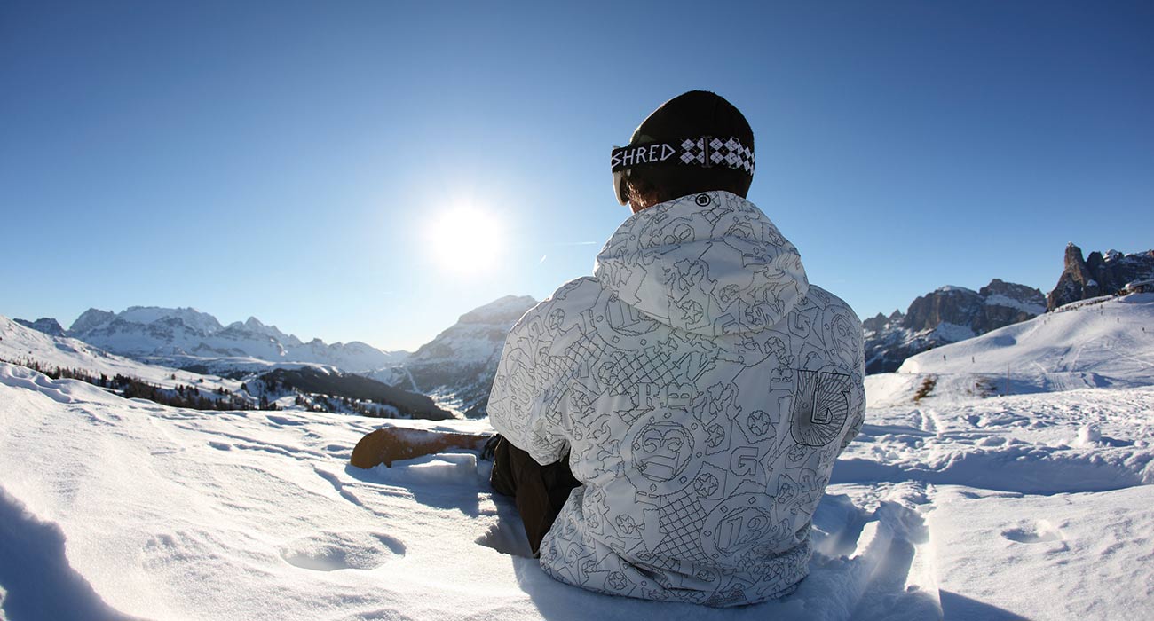 Snowboardfahrer sitzt mitten im Schnee und genießt den strahlend blauen Himmel und die Sonne