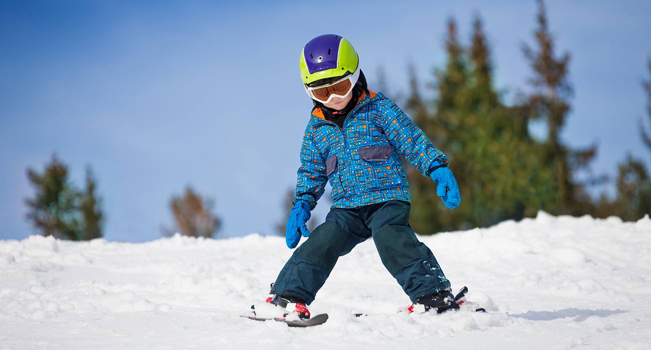 Kleines Kind mit Helm beim Schneepflugfahren auf einer Piste